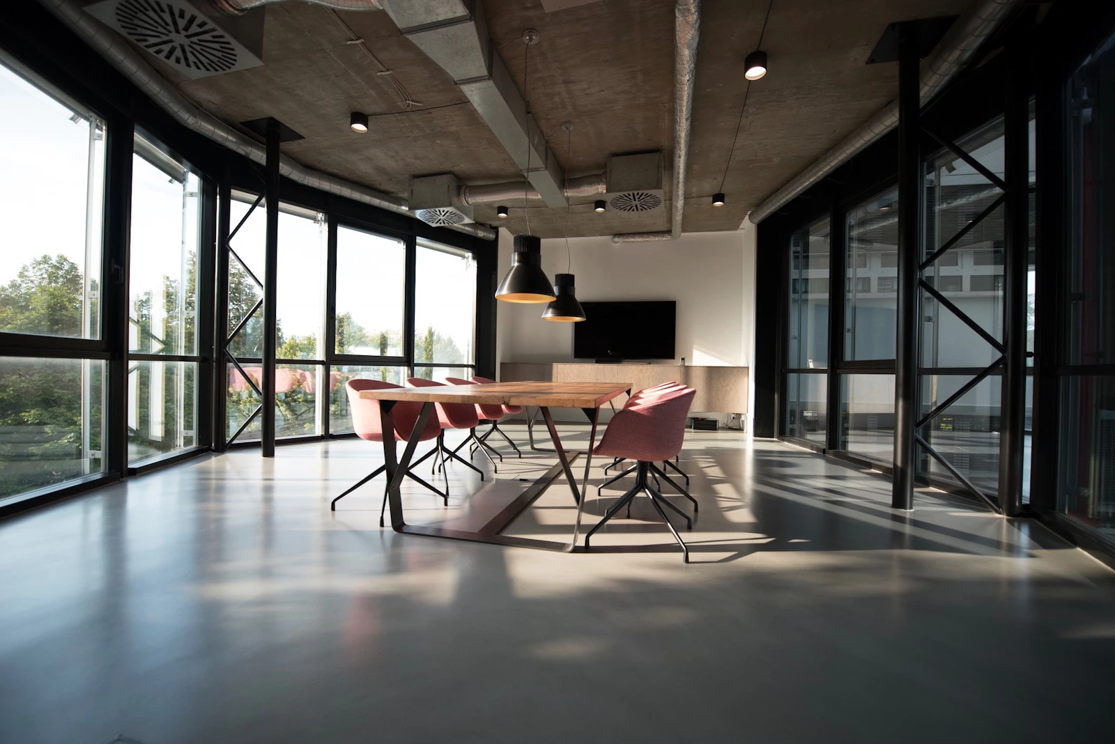 Sala de reuniões de escritório com mesa de madeira, cadeiras e grandes janelas